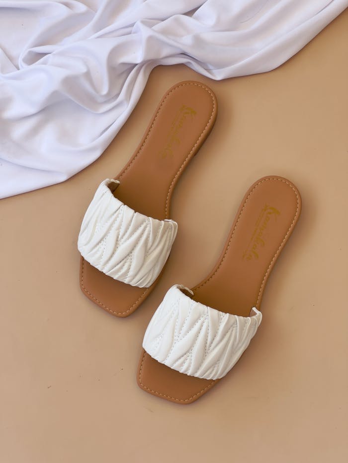 Stylish white quilted slippers on a beige background with white cloth accent.